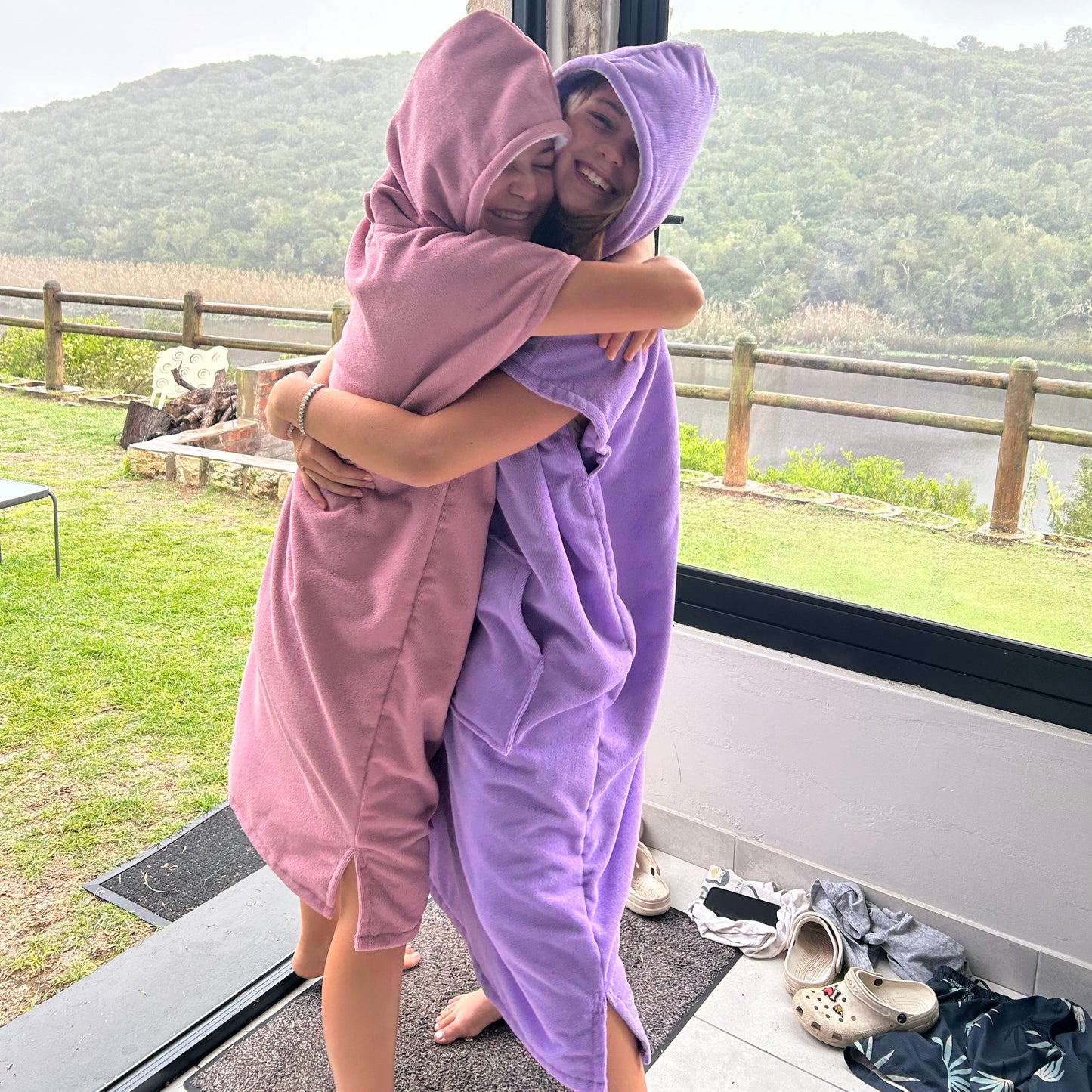 Two girls wearing Octohoodie swimming ponchos in pink and purple at the river