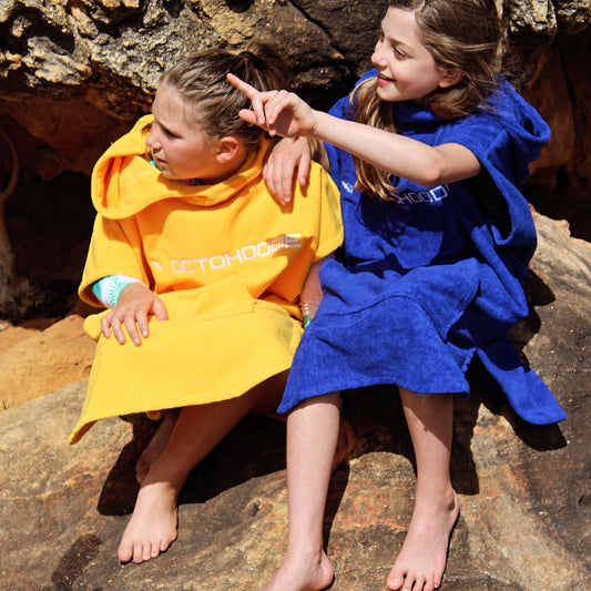 Two children sitting on rocks outdoors, each wearing a short-sleeve Octohoodie.