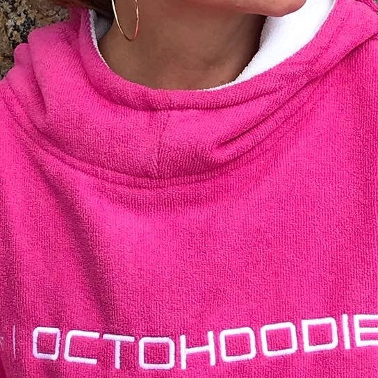Person wearing a pink 'OCTOHOODIE' poncho against a stone wall.