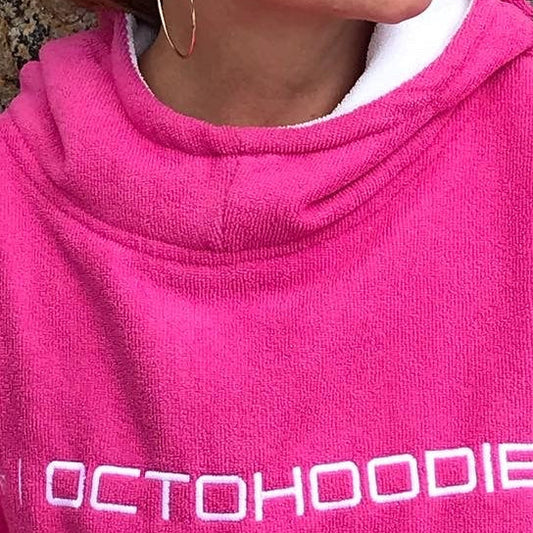 Person wearing a pink 'OCTOHOODIE' poncho against a stone wall.