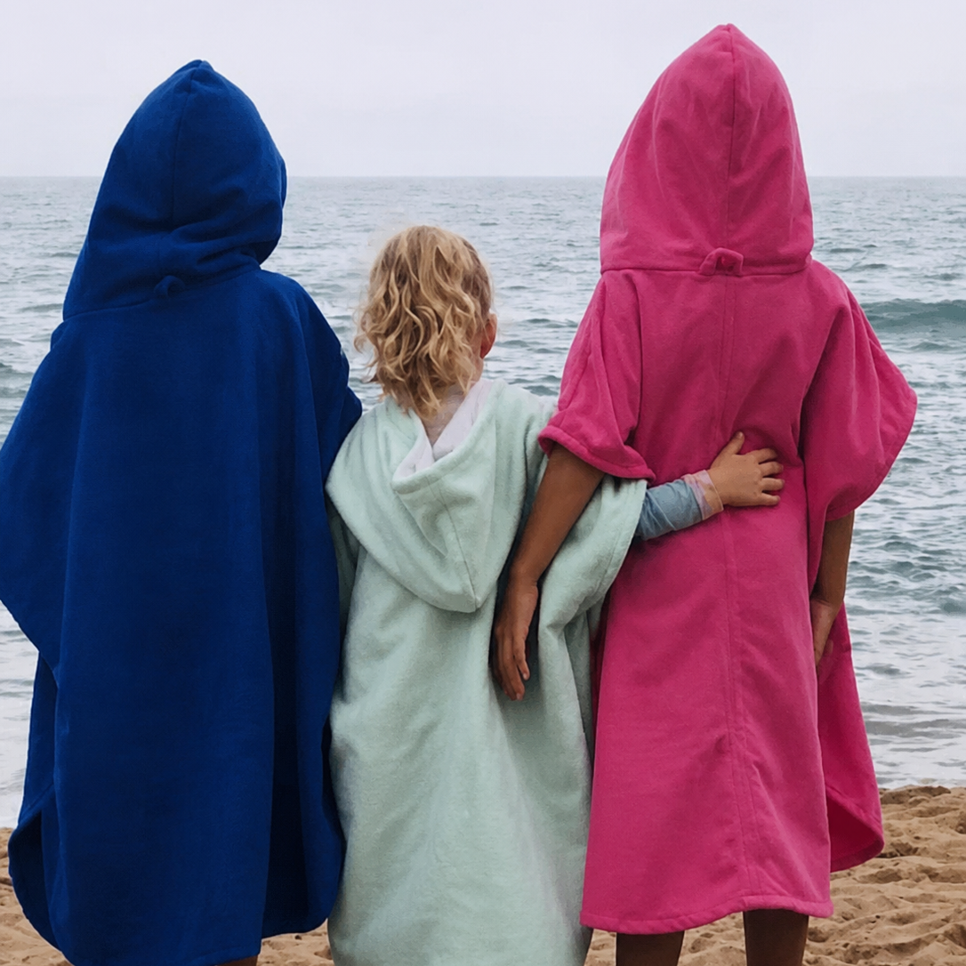 Three children standing on a sandy beach with their backs to the camera, each wearing a hooded Octohoodie short-sleeve