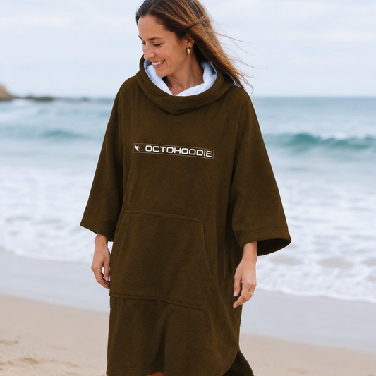 A woman walking on a sandy beach wearing a brown long-sleeve Octohoodie