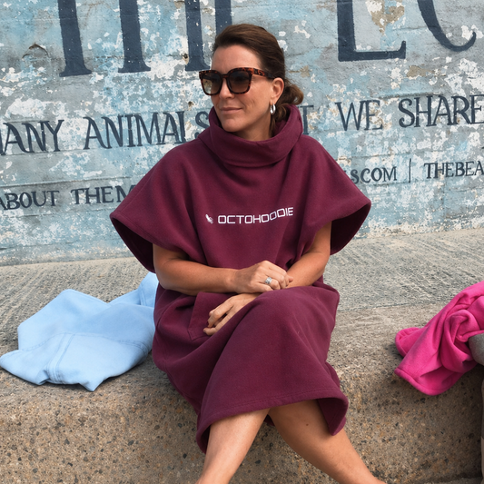 A woman sits on a concrete ledge wearing a short sleeve Mystic Maroon Octohoodie at St James in Cape Town